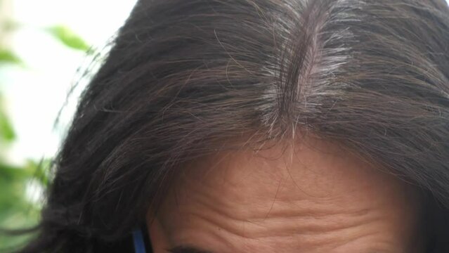 Middle age woman touching her dark hairs with gray color hair roots. Early gray hair, hair loss. Close up