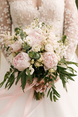 A luxurious wedding bouquet with white and pink peonies in the hands of the bride
