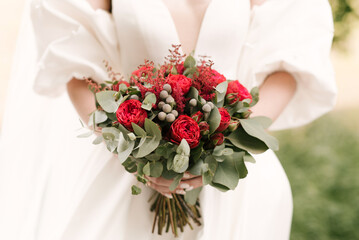 A luxurious wedding bouquet with red roses in the hands of the bride