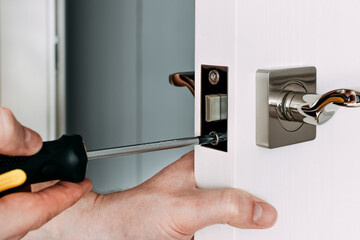 Naklejka premium A locksmith repair the door lock in the room. A locksmith fixing lock with yellow screwdriver. Close-up of repairing door. Selective focus