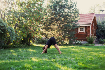 Obraz na płótnie Canvas Over-weighted female doing yoga standing in triangle position on backyard of cottage with wooden house and trees in background. Body positive. Equality. 