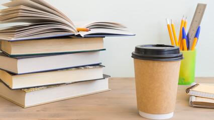 Coffee in a paper cup and a stack of books next to it
