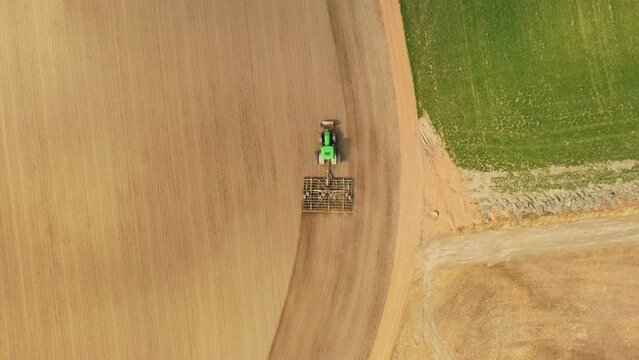 Aerial view rotating above a tractor plowing fields during spring season - overhead, drone shot
