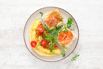 Omelette or omelet, fresh arugula and tomato salad and toasts with butter and salted salmon. Breakfast. Top view