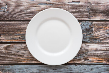 Plate on the background of a wooden tabletop. View from above. Small flat round white plate. Place for text.