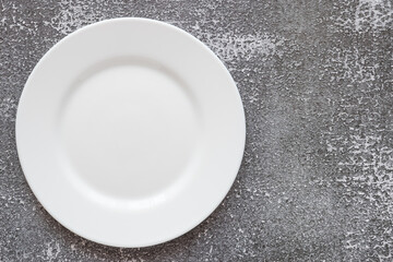 A plate against the background of a marble and concrete countertop. View from above. Small flat round white plate. Place for text.