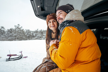 Lovely smiling couple sitting in car trunk in winter forest