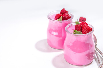Raspberry panna cotta dessert with fresh raspberries and lemon balm mint leaves. Pink panna cotta in small portion jars on a white background