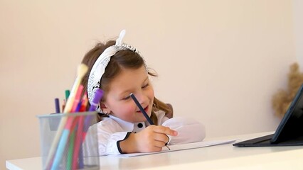 Back to school. Happy little schoolgirl sitting at her Desk. The girl does her homework using a tablet computer. online education. - Powered by Adobe