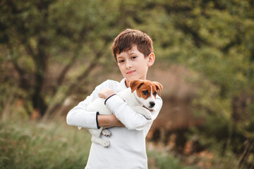 Outdoor portrait of a boy hugging a jack russell terrier puppy. Child loving and caring for a pet