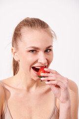 A creative portrait of a beautiful girl holding with one hand a juicy strawberry near her lips with temptation.