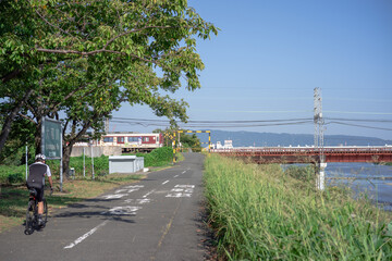 堤防道路をサイクリングする自転車と踏切を通過する電車
