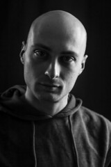 Black and white portrait of a young bald man in the dark with a serious and scary look