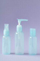 Bottles of travel cosmetics on a purple background, copy space. Set of small empty bottles for cosmetics, side view.