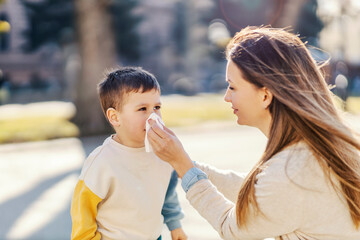 A mother blowing nose to her allergic son in a park.