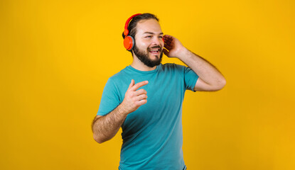 Fototapeta na wymiar portrait of hispanic young man with headphones, dancing and listening music on yellow background in Mexico Latin America
