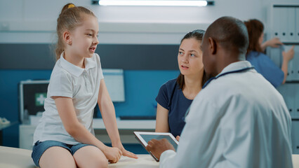 Obraz premium Little kid having discussion with male doctor at examination in medical office. Child and medic talking about health care diagnosis and recovery treatment at checkup visit appointment.