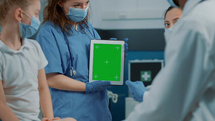 Nurse holding digital tablet with green screen background at checkup visit. Medical assistant using isolated copy space with blank chroma key and mockup template on gadget during pandemic.