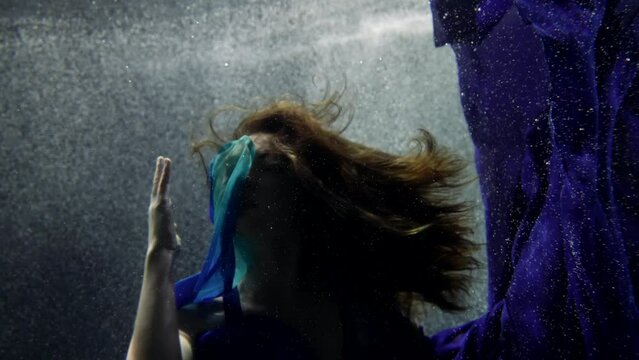 mysterious underwater shot with beautiful young lady playing with silk blue dress, portrait of woman