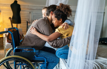 Happy family. Smiling father with disability in wheelchair hugging with children at home
