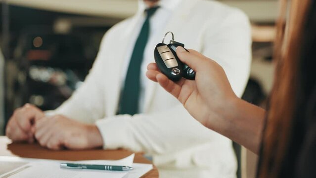 Closeup keys from new luxury auto. Competent car dealer sitting with buyers at desk, making contract and giving keys from new luxury auto. Unrecognizable Woman buying new vehicle at showroom