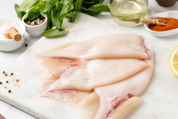 Raw squid and ingredients on the table. Preparation of raw squid fillet. Seafood background, concept. White board.