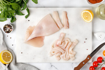 Preparing seafood. Raw squid and ingredients on white marble table with lemon and pepper. Top view.