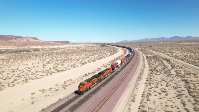 A freight train rolling down the track in a desert landscape - aerial view of the engine pulling cars that disappear into the distance