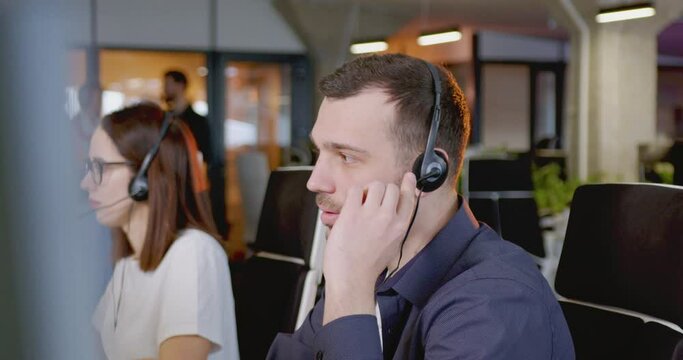 Caucasian young man in headset talking with client at computer. Call center concept. Portrait of happy male support worker looking at camera and smiling. Job in sales. Selling by phone.