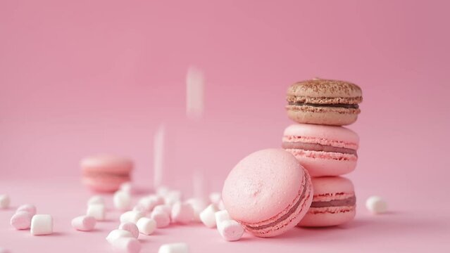 French delicacy sweet pink macaroons with falling fluffy marshmallows isolated at pink background. ConFrench delicacy sweet pink macaroons with falling fluffy marshmallows isolated at pink background