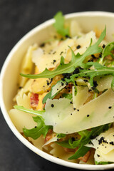 Pasta with chicken, cream sauce, parmesan and greens in a round paper takeaway food container on a dark background. Concept of take-away and healthy food delivery.