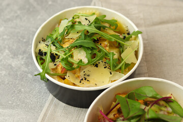 Pasta with chicken, cream sauce, parmesan and greens in a round paper takeaway food container on napkin on a gray background. Concept of take-away and healthy food delivery.