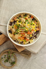 Healthy bowl with wild rice, chicken and vegetables on wooden board on gray background. Food delivery service and daily ration concept.
