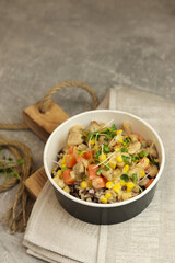 Healthy bowl with wild rice, chicken and vegetables on wooden board on gray background. Food delivery service and daily ration concept.