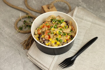 Healthy bowl with wild rice, chicken and vegetables on wooden board on gray background. Food delivery service and daily ration concept.