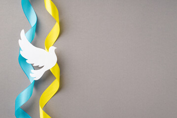 Stop the war in Ukraine concept. Top view photo of national flag curly ribbons and white pigeon silhouette on isolated grey background with copyspace