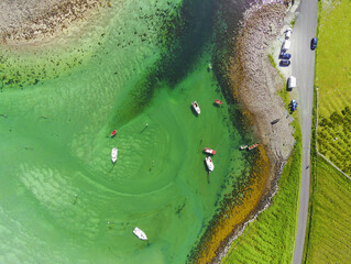 Aerial top down view on a small boats and yachts and car park with cars and small country road by green fields. Warm sunny day. Water sports and fishing hobby concept.