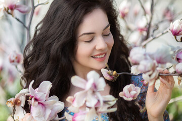 Beautiful girl with flowers of magnolia. Portrait of young smiling brunette woman under blossom...