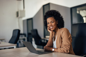 Smiling African woman, holding hand on her chin while posing for the camera at the office.