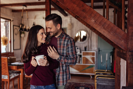 Woman and man in a hug, spending the weekend at their wooden cottage.