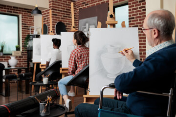 Senior paralyzed man in wheelchair attenting art class drawing vase sketch on white canvas...