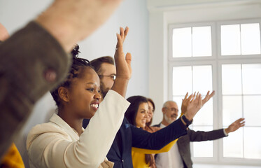 Diverse male and female audience standing in row and raising hands up. Indoor shot of happy mixed...