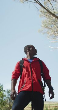 Vertical video of happy african american man hiking in countryside, taking a break and enjoying view