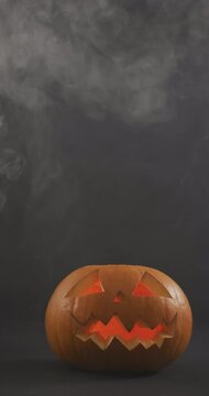 Vertical video of lit carved halloween pumpkins with clouds of smoke on grey background
