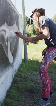 Vertical video of caucasian hipster male artist with long hair painting whale mural on wall