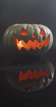 Vertical video of close of lit carved halloween pumpkin on grey background