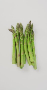 Vertical video of fresh stalks of asparagus on white background