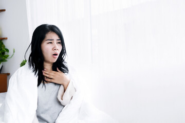 Asian woman having sore throat sitting in bed in the morning hand holding her neck pain