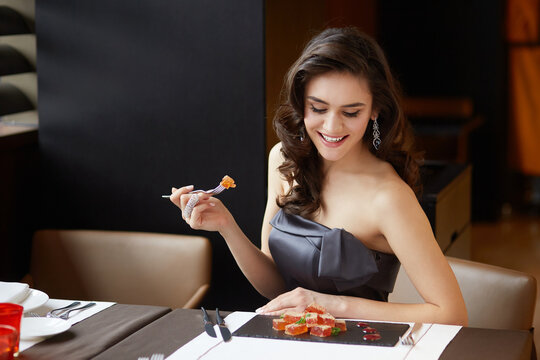 Sensual brunette in an evening dress, serves a dessert in the restaurant, dressed in a dress with bare shoulders, makeup and hairstyle.