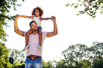 Obraz premium Portrait of happy black father carrying daughter on back outdoors. Family happiness love concept.